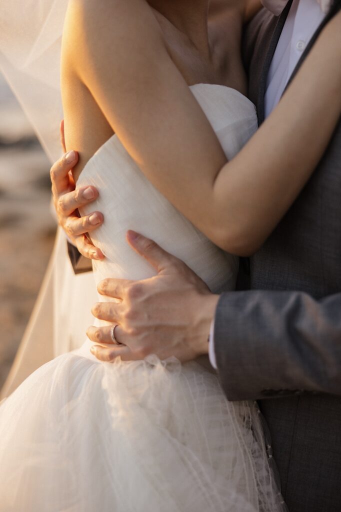 Close up photo of a bride's torso being held by the groom, on the groom's hand is his wedding ring