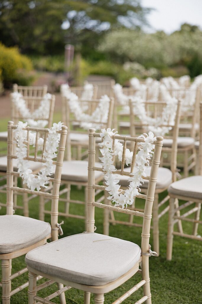 Detail photo of a chair surrounded by other chairs each with a white flower lei on them ready for a wedding ceremony