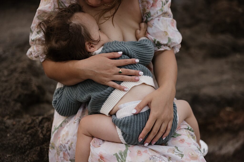 A child breastfeeds from their mother during a family session at Makapuu Lookout on Oahu