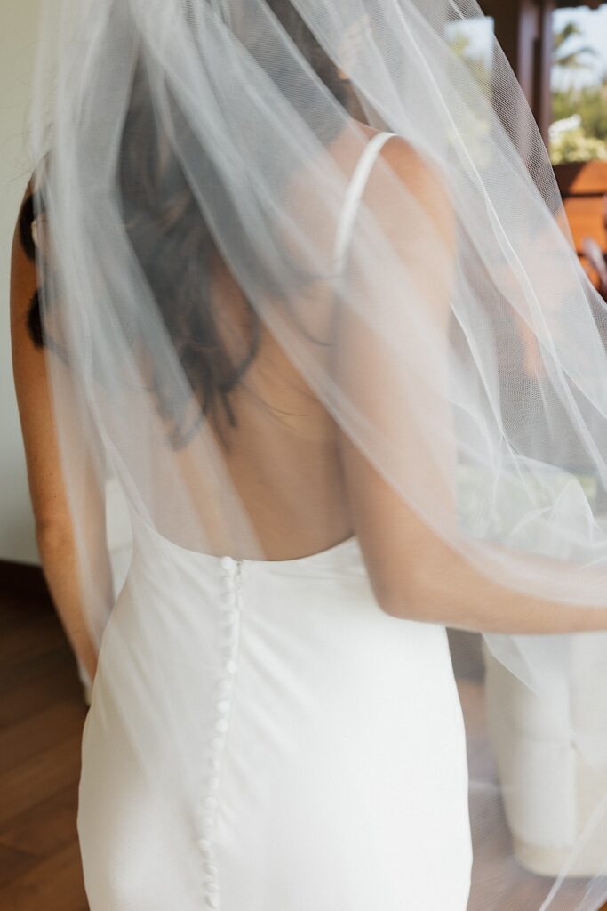 A bride facing away from the camera plays with her veil