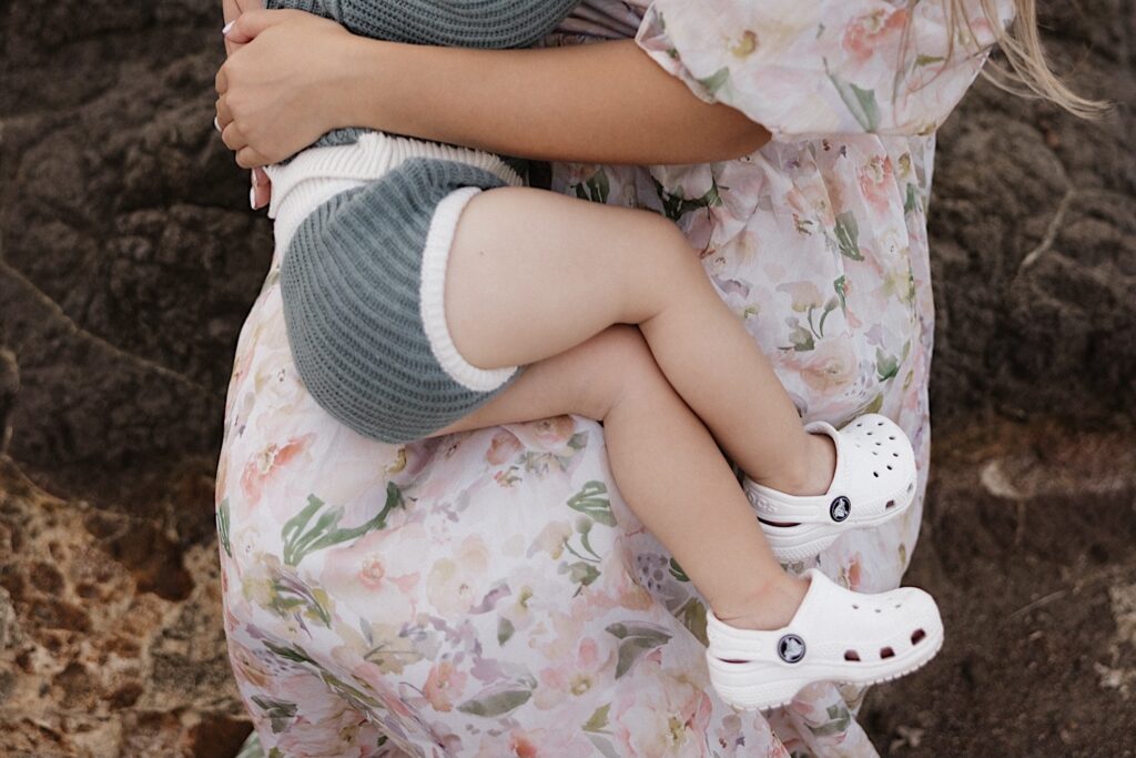 Close up photo of a young child sitting on their mother's lap while the mother sits on a rock