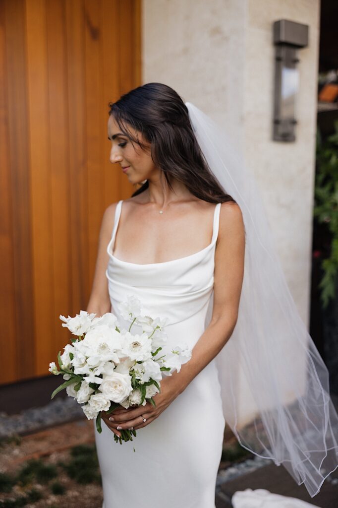 A bride smiles and looks down and to the left while holding a bouquet of white flowers