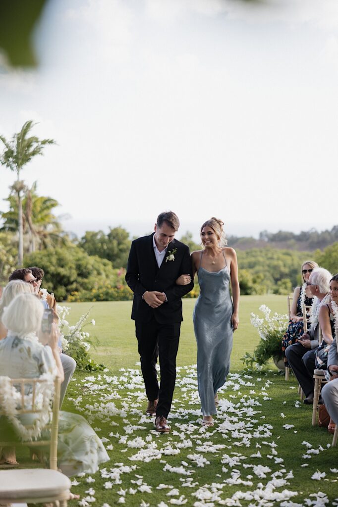 A bridesmaid and groomsman walk down the aisle together and smile as guests on either side watch