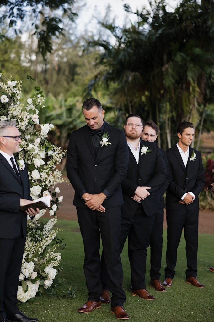 A groom smiles and looks down during his wedding ceremony with his groomsmen standing behind him