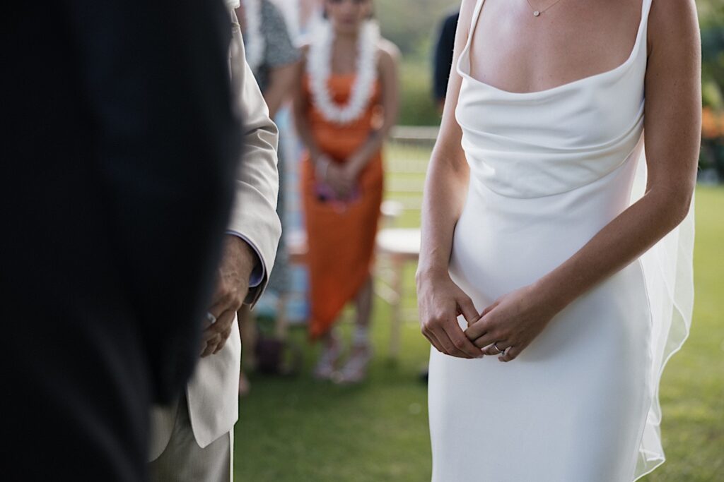 A bride holds her hands while standing in front of the groom during her wedding ceremony on the island of Kauai