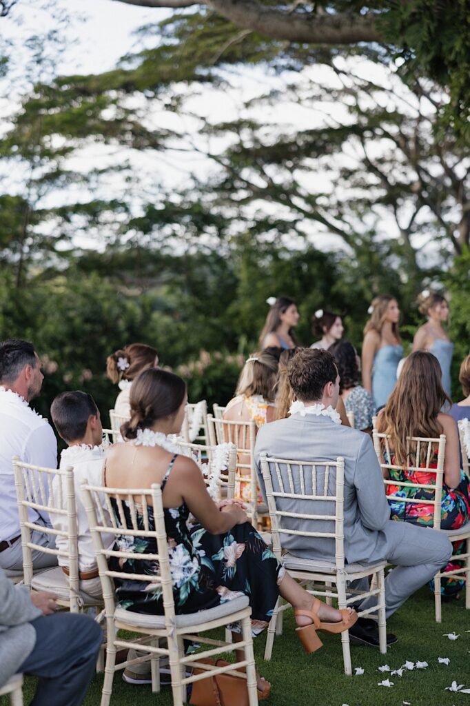 Guests of a Hawaiian wedding sit in chairs and watch as the ceremony begins
