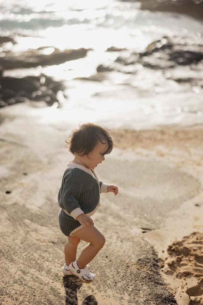 A young child runs along the beach in their crocs with water in the background