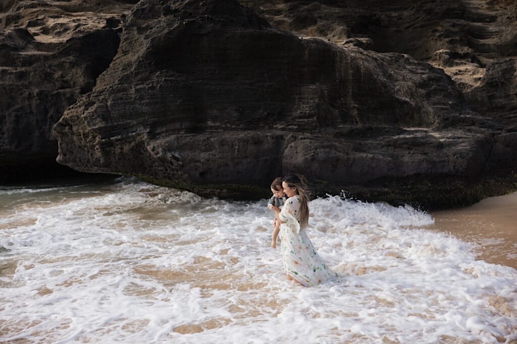 During a family session a mother holds her young child as she walks into the water of a beach near Makapuu Lookout on Oahu, the child is looking down at the water