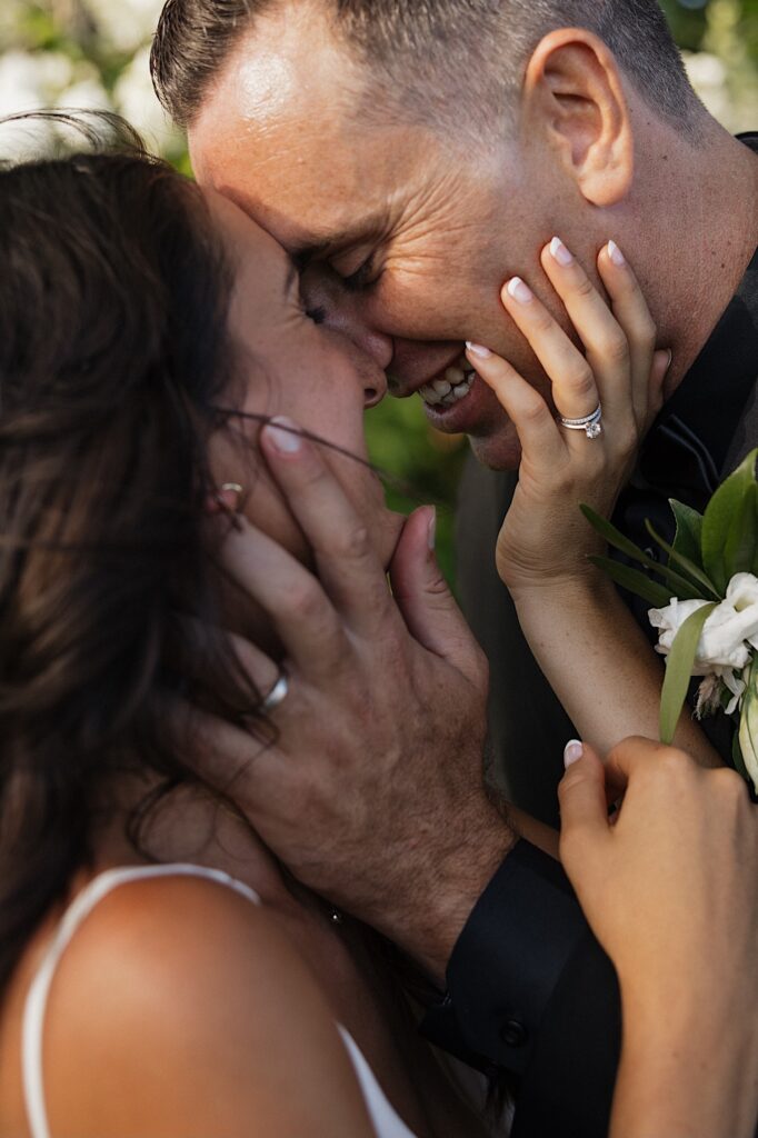 Closeup photo of a bride and groom smiling as they grab each other's face and are about to kiss
