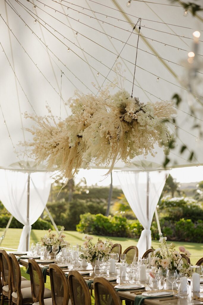 White flowers hang from a tent covering a wedding reception space