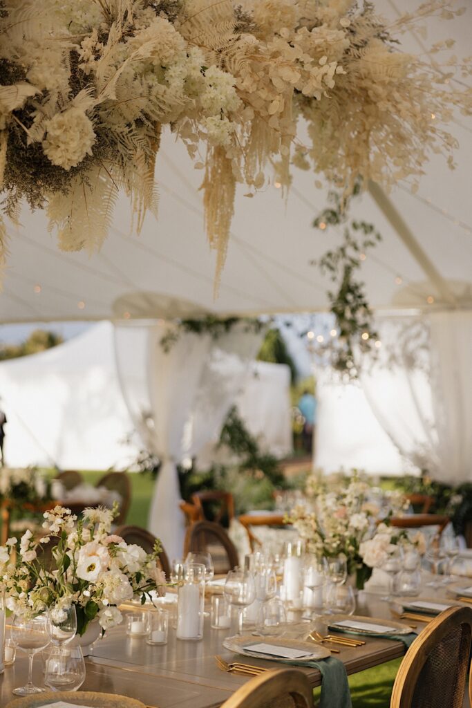 Flowers hang above a table decorated for a wedding reception underneath a tent