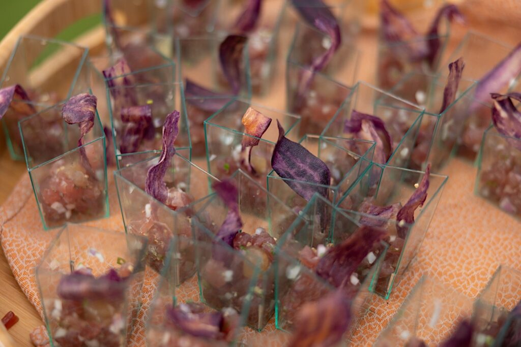 Square glasses sit on a table filled with purple flower garnish
