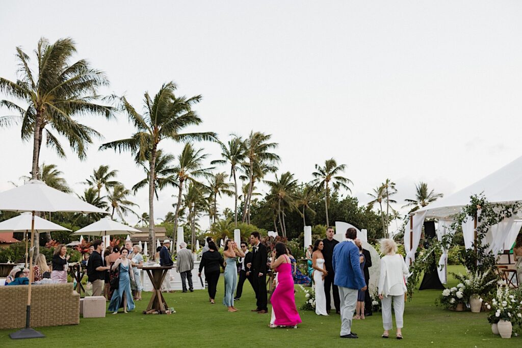 Guests of an outdoor wedding reception mingle during cocktail hour at Kukui’ula on Kauai