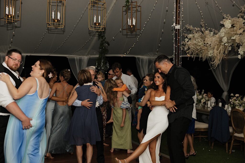 A bride and groom dance together with guests of their wedding reception under a tent at Kukui’ula on Kauai