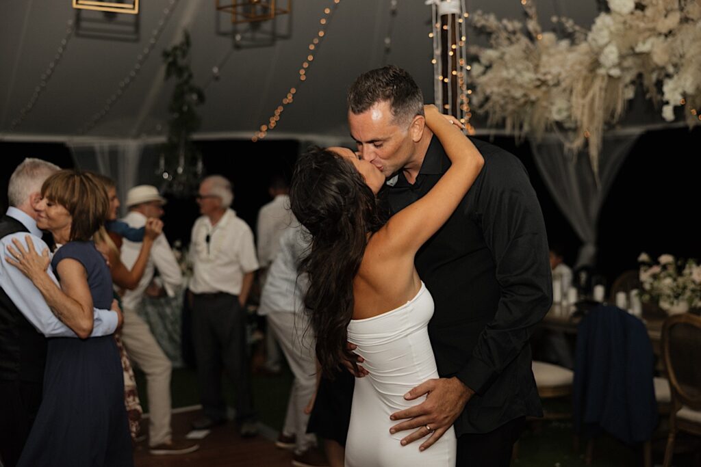 A bride and groom kiss one another while guests of their wedding reception dance around them at Kukui’ula on Kauai