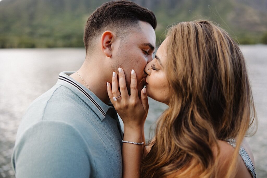 A man and woman kiss while the woman shows off her ring after a proposal on a dock at Secret Island on Oahu