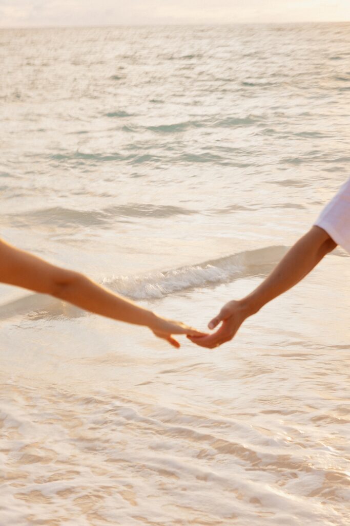 A pair of hands reach out to one another with the waves of the ocean behind them