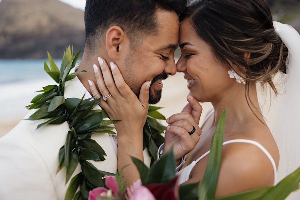 A bride and groom smile at one another as they touch faces after their first look on their wedding day in Hawaii