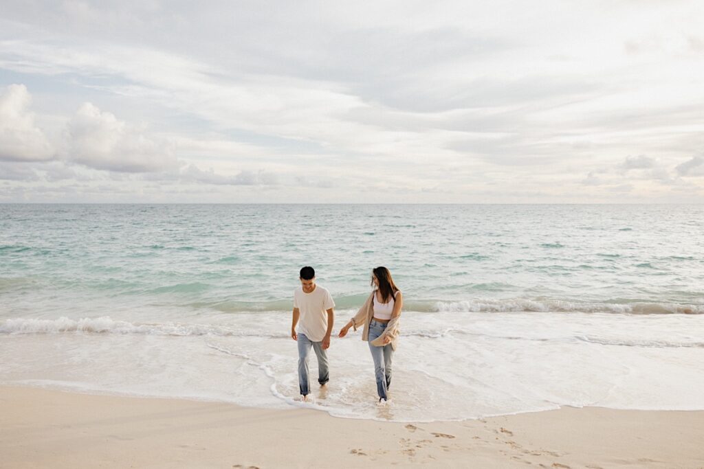 A man and woman walk next to one another away from the ocean towards the camera during their engagement photos session on Oahu
