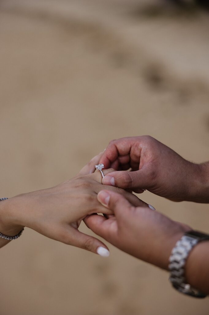 A man puts an engagement ring on the hand of a woman on a sandy beach