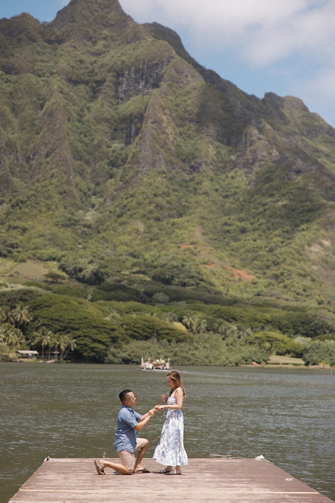 A man proposes while on a dock looking out over a lake with a mountain in the background in Oahu