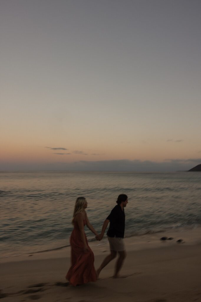 A man and woman walk hand in hand along a beach as the sun rises