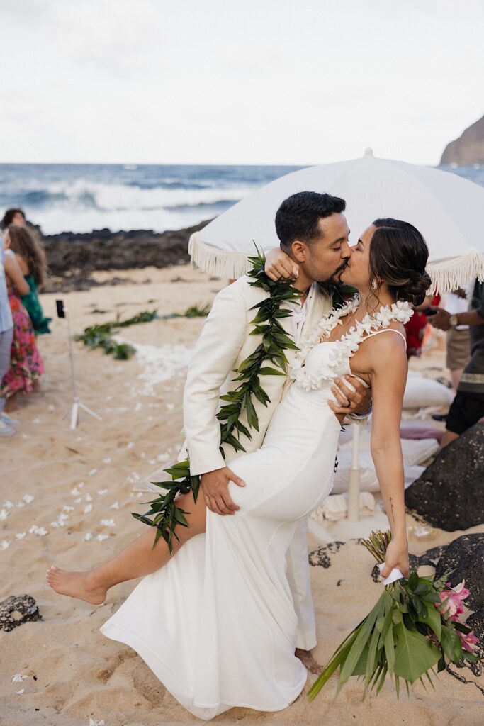 A bride and groom kiss during their wedding ceremony on a beach of Oahu