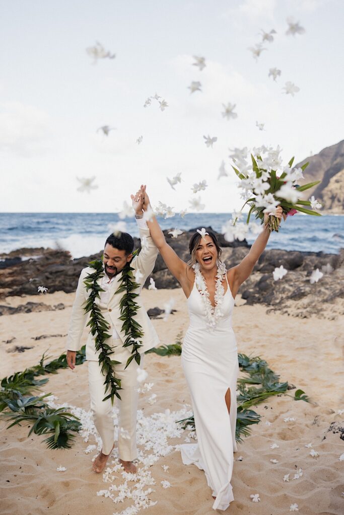 A bride and groom cheer as they exit their wedding ceremony of a beach of Oahu