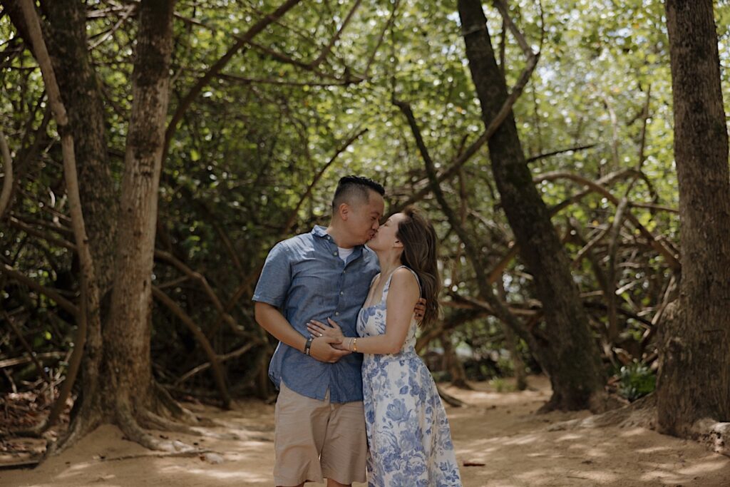 A man and woman kiss while in a forest after their surprise proposal on the island of Oahu