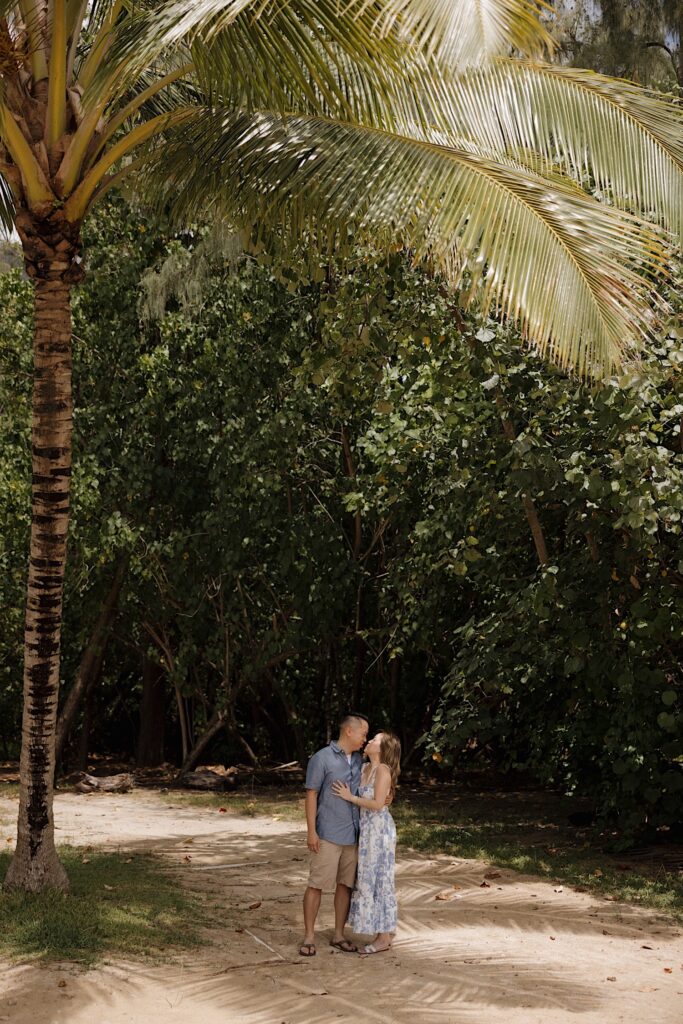 A man and woman embrace and kiss one another while under a palm tree