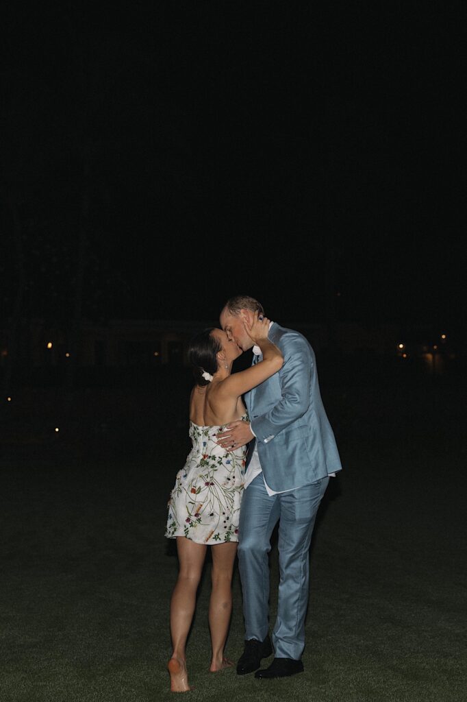 A bride and groom kiss one another while walking along a beach at night