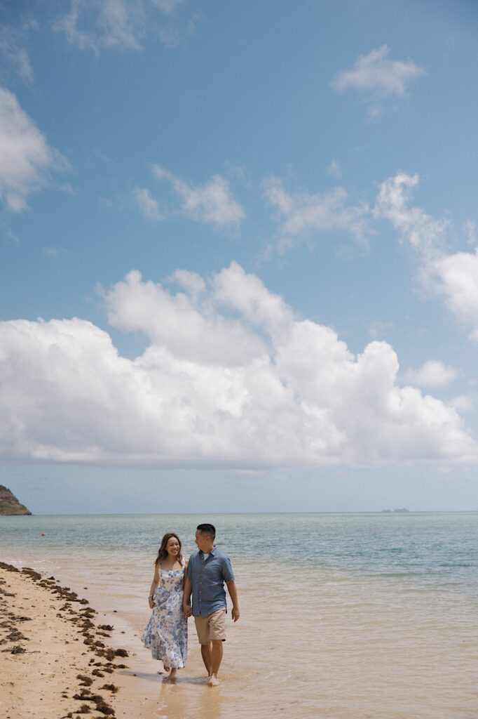 A man and woman walk along a beach while holding hands on the island of Oahu