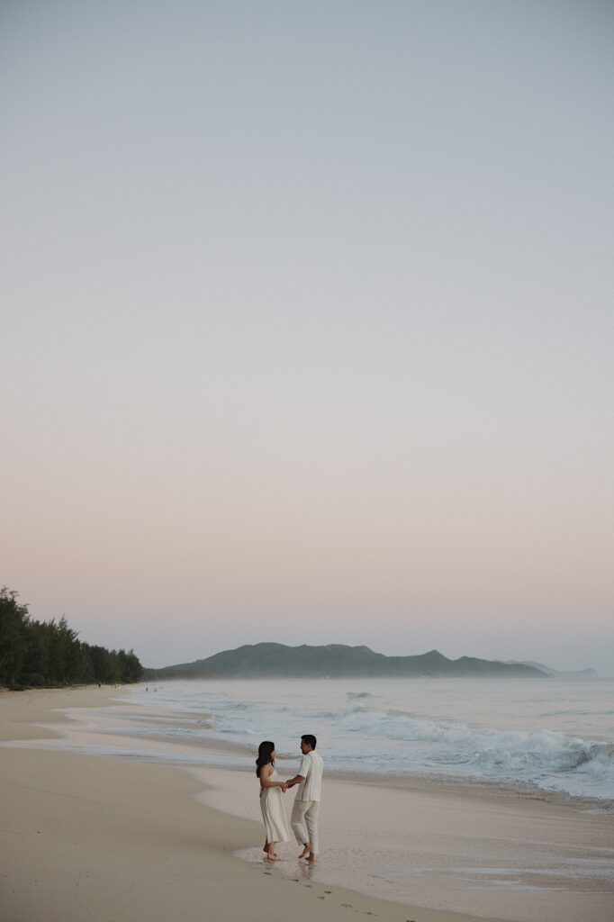 A couple face one another while holding hands on Waimanalo Beach on Oahu as the sun begins to rise