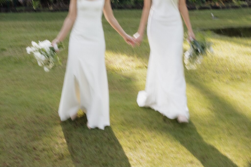 Blurry photo of two brides walking towards the camera while holding hands in a field of grass