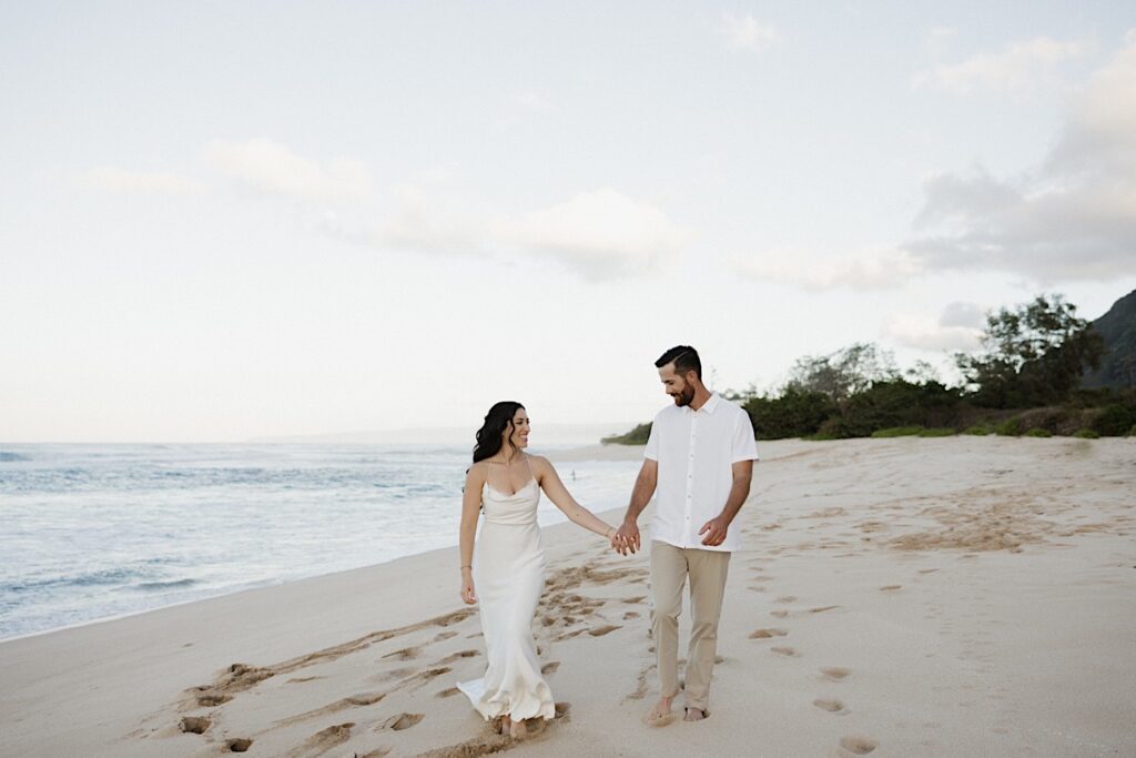 A bride and groom walk hand in hand along a beach in Hawaii to celebrate their elopement