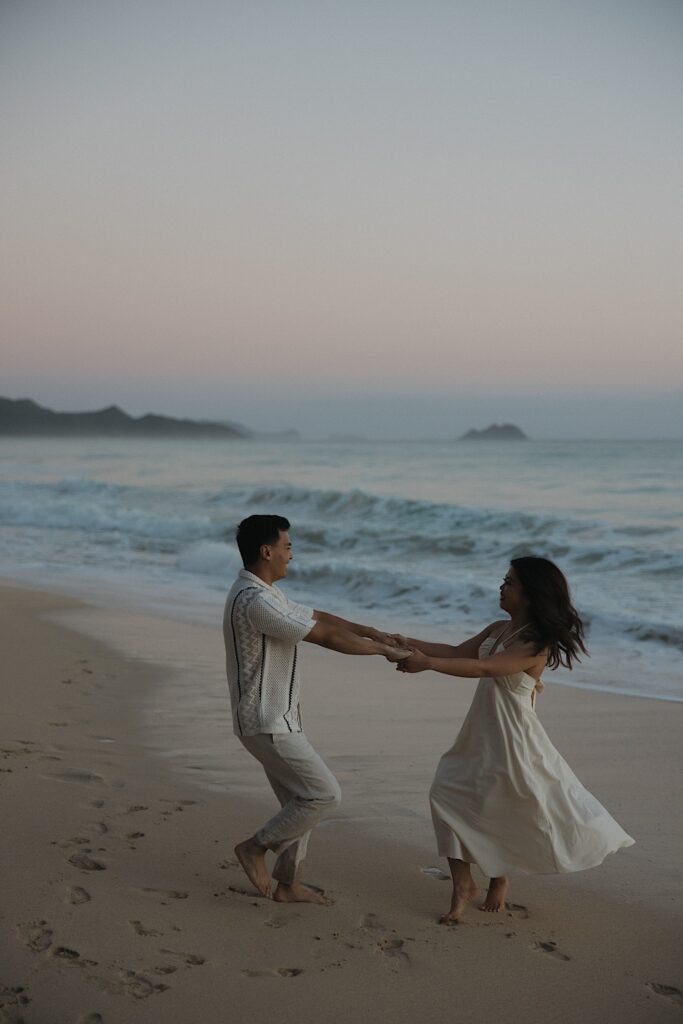 A couple hold hands while spinning and dancing together on Waimanalo Beach on Oahu as the sun rises