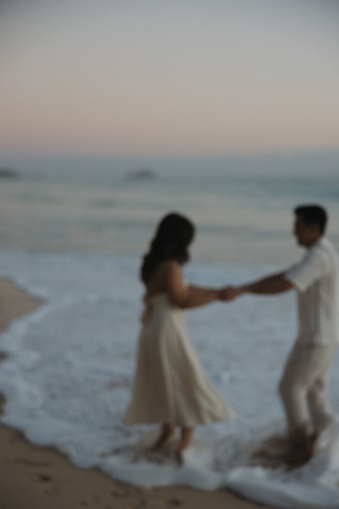 Out of focus photo of a man and woman holding hands with their feet in the water while at Waimanalo Beach on Oahu