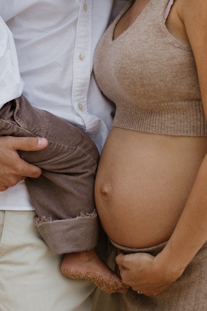 Close up photo of a mother's pregnant belly, standing next to her is a man who is holding their other child