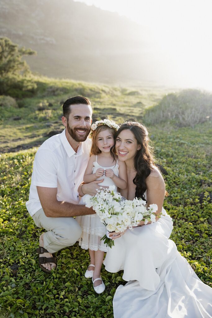 A bride and groom crouch next to their flower girl while on a mountain in Hawaii