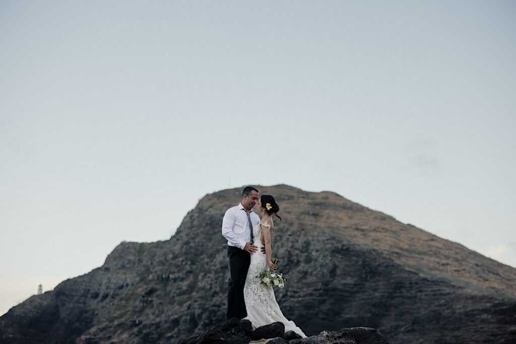 A bride and groom embrace one another while standing on a rock with Makapuu Lookout behind them during their elopement in Hawaii