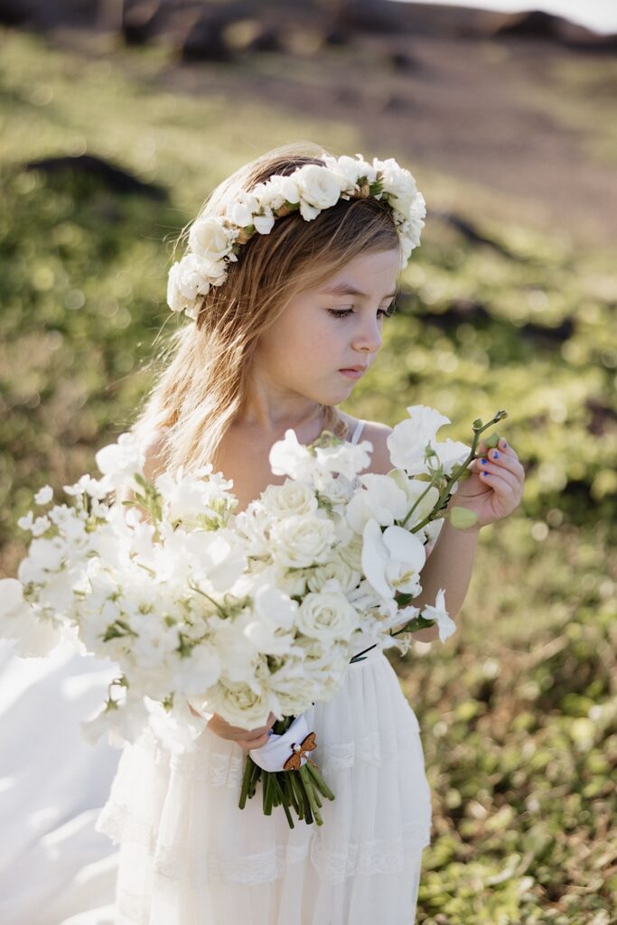 A young flower girl stands and stares at her bouquet of flowers