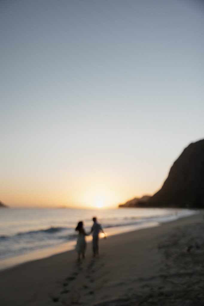 Out of focus photo of a couple walking along Waimanalo Beach on Oahu towards the sunrise