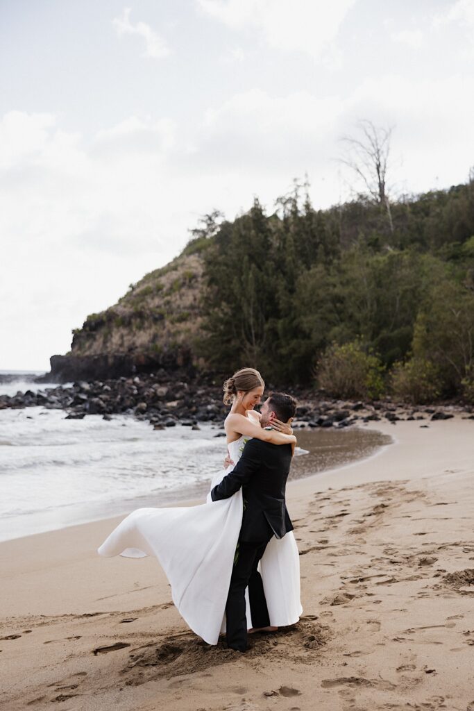 A bride and groom on a beach in Hawaii dance together next to the ocean