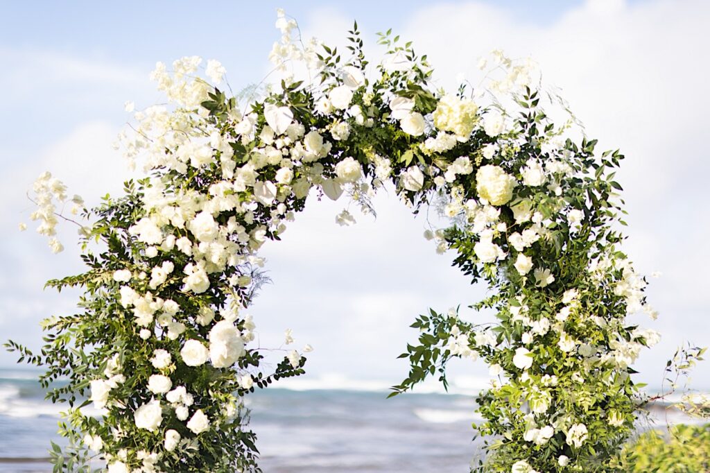 A white floral altar in front of the ocean on a sunny day