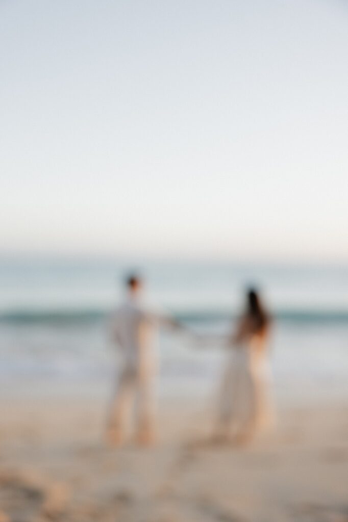 Out of focus photo of a couple standing next to the ocean while holding hands at sunrise