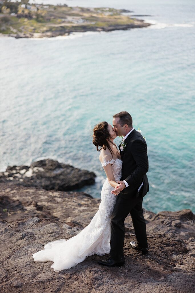 A bride and groom kiss one another while standing atop Makapuu Lookout in Hawaii