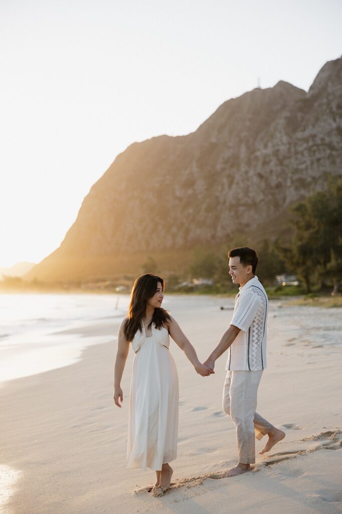 A couple hold hands while the woman looks back over her shoulder towards the man as they walk along Waimanalo Beach on Oahu