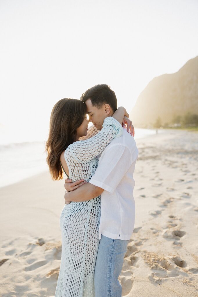 A couple embrace and touch their foreheads together while the sun rises behind them over Waimanalo Beach