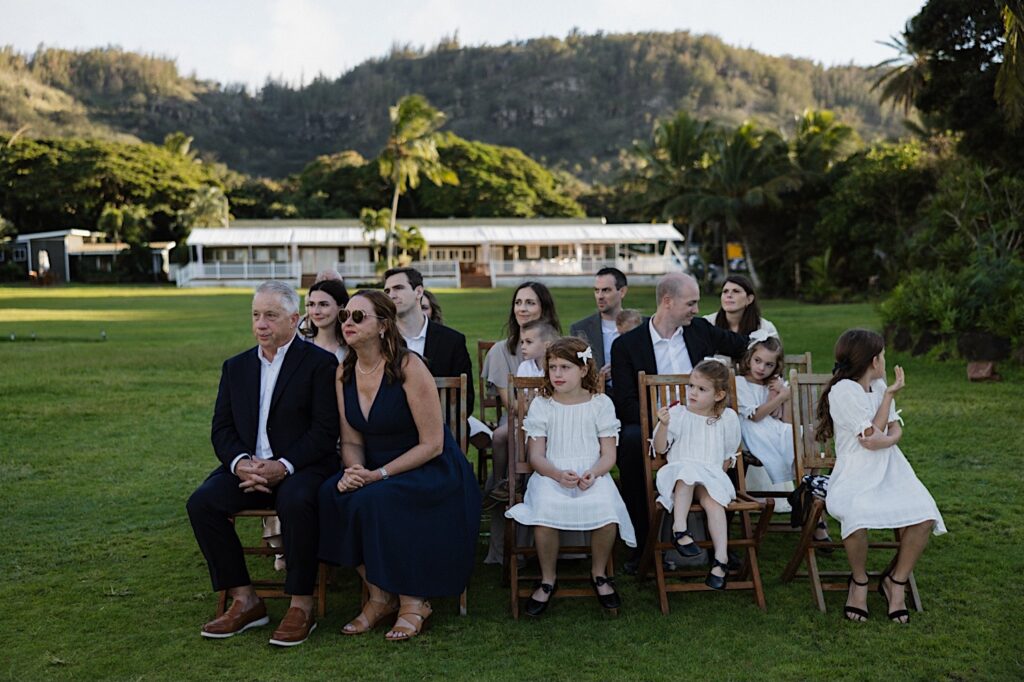 Guests of an intimate LGBTQ wedding ceremony sit as the outdoor ceremony at Loulu Palm on Oahu takes place while the sun sets
