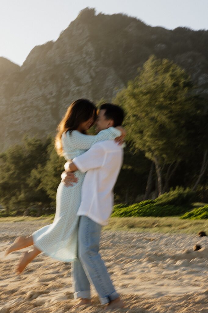 Blurry photo of a couple hugging and spinning on Waimanalo Beach on Oahu with a mountain behind them